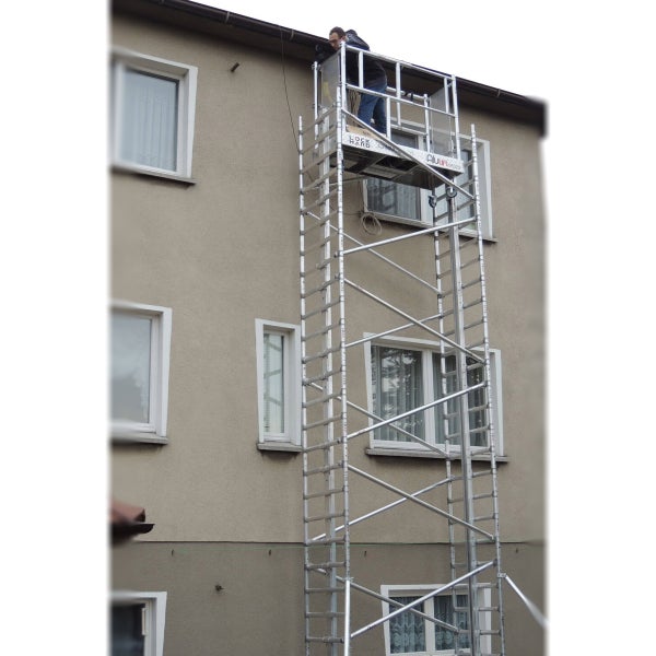 Eine hohe, fahrbare Arbeitsbühne aus Aluminium steht an einer Hauswand, auf der eine Person arbeitet.