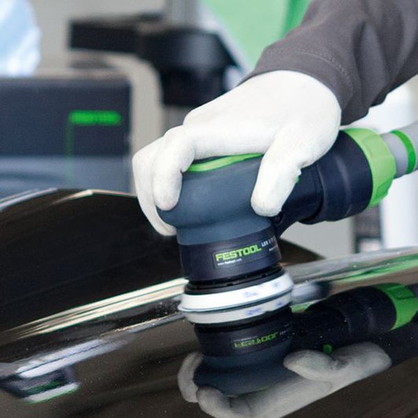 Festool Logo. Hand mit Handschuh bedient Exzenterschleifer auf einer Oberfläche.