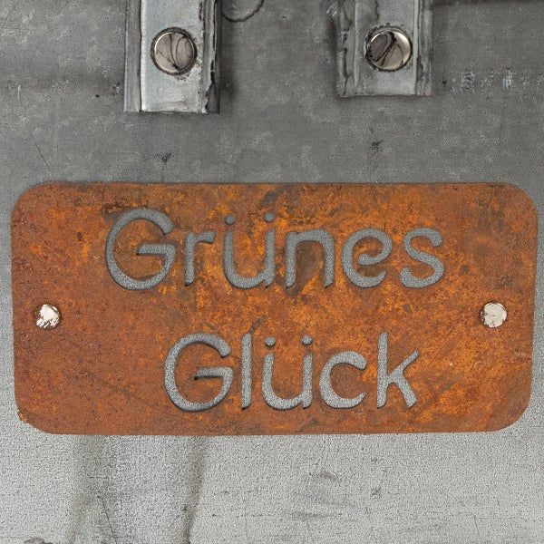 Rostiges Metallschild mit der Aufschrift Grünes Glück, Garten-Deko aus Metall in Edelrost-Optik.