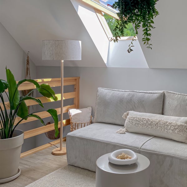 Heller Wohnbereich im Dachgeschoss mit einem texturierten Sofa, Beistelltisch, Stehlampe und Zimmerpflanzen in natürlicher Einrichtung.