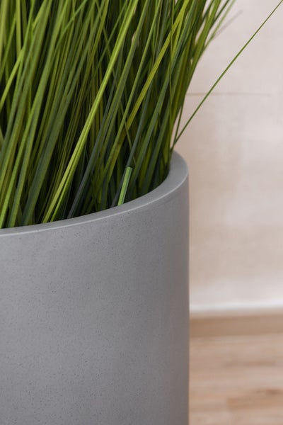 Künstliches Gras in einem grauen, zylindrischen Pflanztopf mit glatter Oberfläche zur Dekoration.