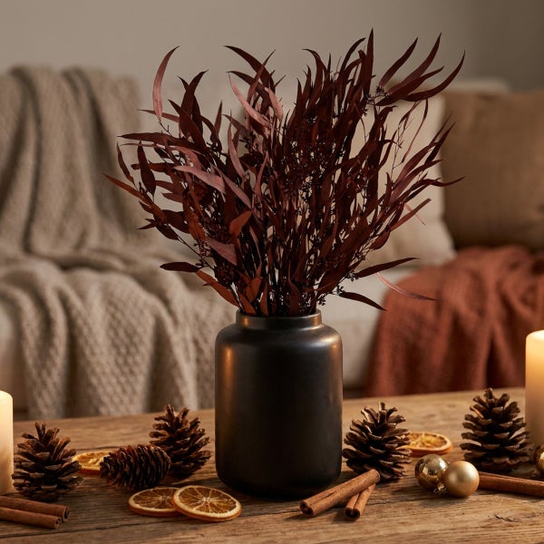 Dunkle Vase mit getrockneten Zweigen, Tannenzapfen, Zimtstangen und getrockneten Orangenscheiben als winterliche Tischdekoration auf Holz
