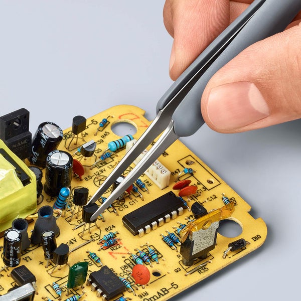 Elektronikpinzette in der Hand über einer Leiterplatte mit elektronischen Bauteilen