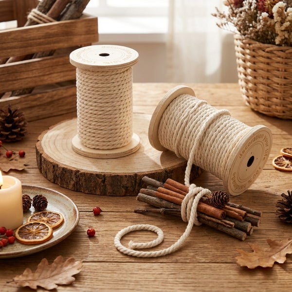 Zwei Garnrollen mit Baumwollschnur auf einem Holztisch mit herbstlicher Dekoration aus Zimtstangen, Kiefernzapfen und getrockneten Orangenscheiben.