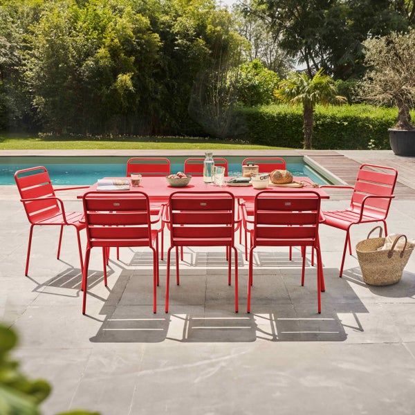 Gartenmöbel-Set auf einer hellen Terrasse am Pool, bestehend aus einem roten Metalltisch und passenden Stühlen, gedeckt für eine Mahlzeit.