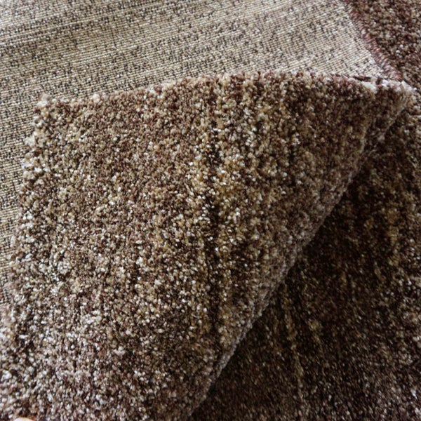 Nahaufnahme eines braun melierten Hochflor-Teppichs mit einer umgeschlagenen Ecke, die den gewebten Rücken zeigt.