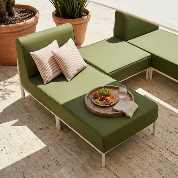 Modulares Garten-Lounge-Set mit grünen Polstern, weißem Gestell, gestreiften Kissen und Obsttablett auf einer Steinterrasse mit Pflanzen.
