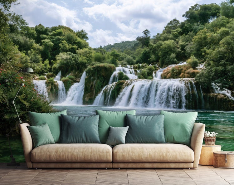 Wohnzimmer mit Fototapete eines Wasserfalls, beiges Sofa mit vielen Kissen, Holzfußboden und Stehlampe, natürliche und entspannte Atmosphäre.