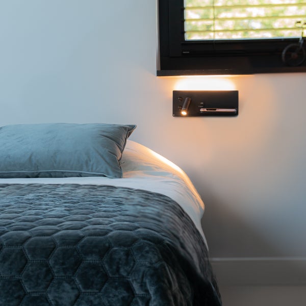 Nahaufnahme eines Bettes mit einer Wandleuchte mit Leselampe und Ablagefläche