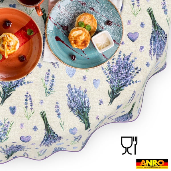 Tischdecke mit Lavendel-Motiv und Herzen, gedeckt mit Tellern. Helle Szene, rustikaler Stil, lebensmittelecht. ANRO Deutsche Manufaktur Logo.