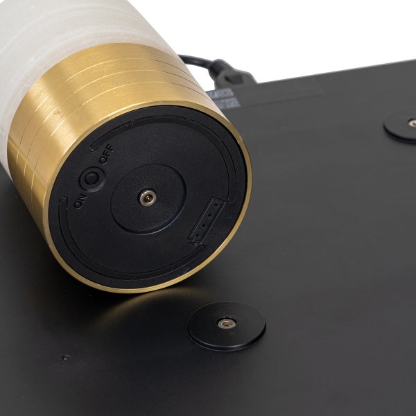 Detailansicht der Unterseite einer zylindrischen LED Tischleuchte mit goldfarbenem Sockel, Ein und Ausschalter und Ladekontakt auf einer Ladestation.