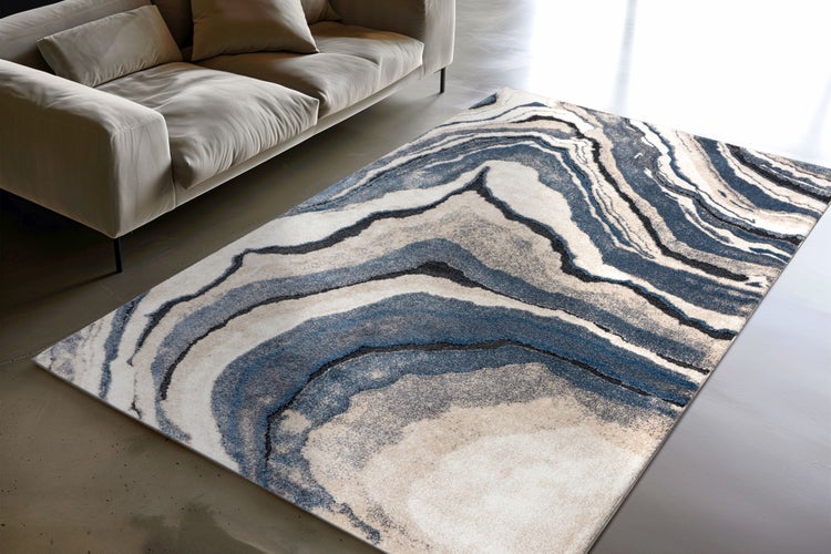 Moderner Wohnzimmerteppich mit abstraktem, wellenförmigem Design in Steinoptik, platziert vor einem Sofa in einem hellen Wohnbereich.