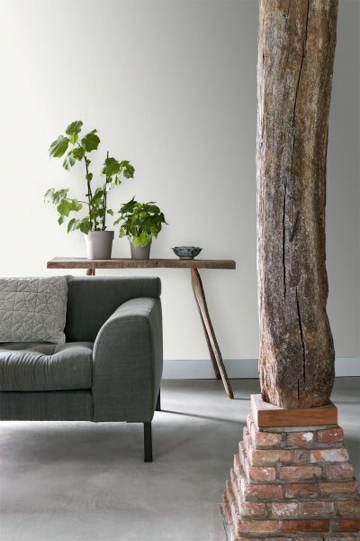 Wohnzimmer mit grauem Sofa, Holztisch mit Pflanzen und dekorativer Holzsäule auf Backsteinsockel