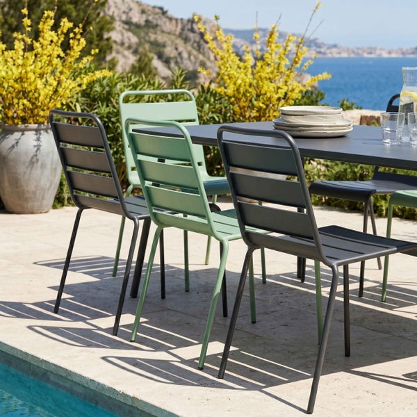 Moderne Gartenstühle und ein Gartentisch aus Metall auf einer hellen Terrasse an einem Pool mit Meerblick.