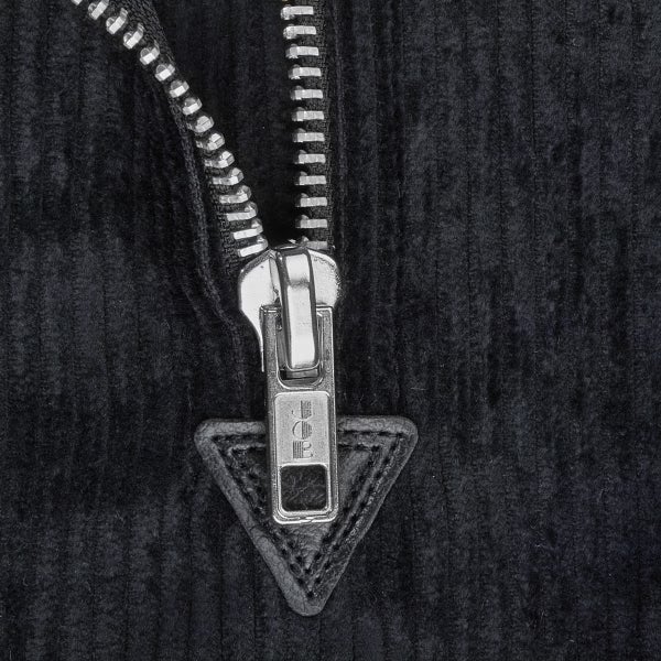 Nahaufnahme eines Metallreißverschlusses an Cordstoff mit eingraviertem Schriftzug auf dem Schieber.