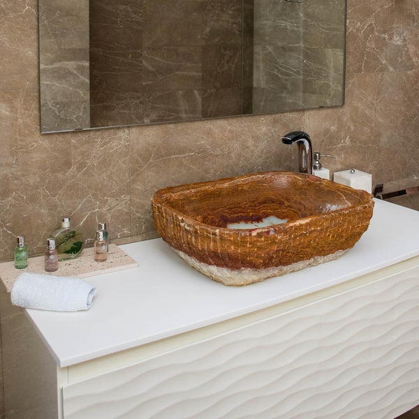 Rustikales Aufsatzwaschbecken aus Naturstein auf einem weißen Waschtischunterschrank in einem Badezimmer mit Marmorfliesen.