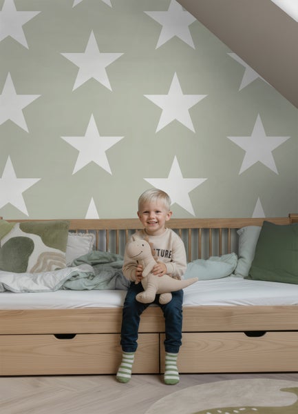 Helles Kinderzimmer mit Sternen-Vliestapete, einem Holzbett mit Schubladen und einem Kind mit Stofftier.