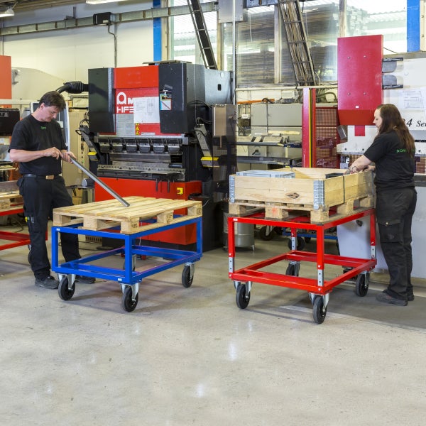 Zwei Mitarbeiter in einer Fabrikhalle mit Palettenwagen und Werkzeugmaschine