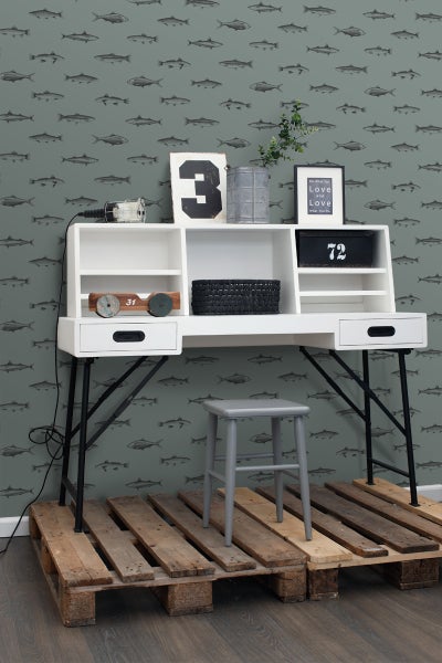 Szene mit einem Schreibtisch mit Regalen, Schubladen und einer grauen Hocker auf Holzpaletten vor einer Tapete mit Fischmuster.