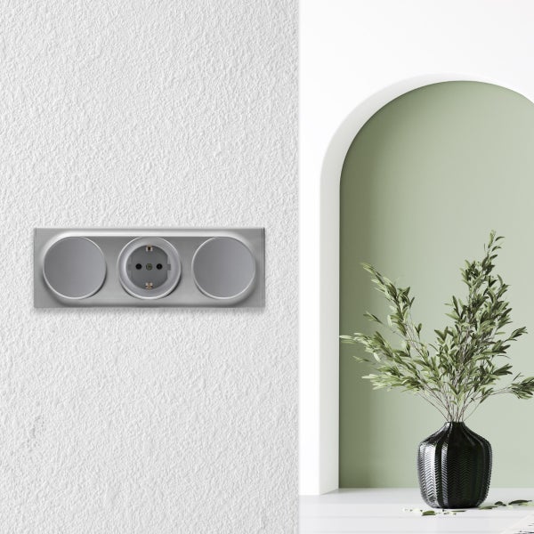 Dreifach Steckdosenrahmen mit einer Schuko Steckdose an einer Wand neben einer Nische mit einer Vase