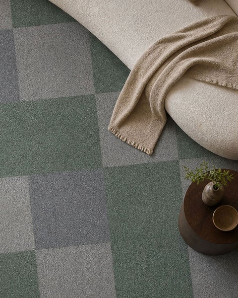 Teppichfliesen im Schachbrettmuster in einem modern eingerichteten Wohnzimmer mit Sofa und hölzernem Beistelltisch.
