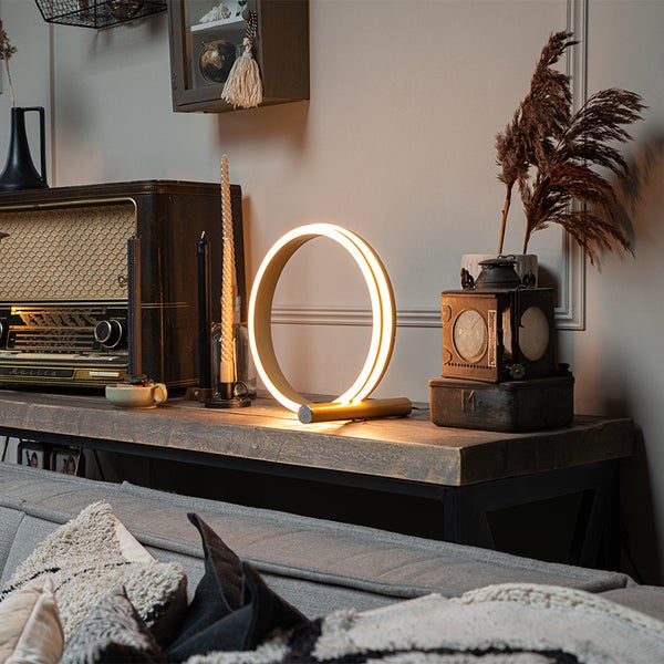 Dekorative Ringschreibtischlampe auf einem Holztisch neben anderen Dekorationen.