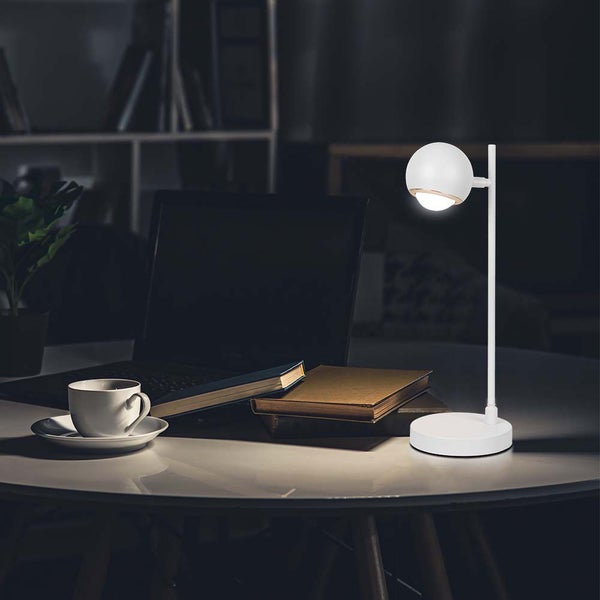 Tischszene mit Lampe, Laptop, Büchern und Kaffeetasse auf einem Tisch.