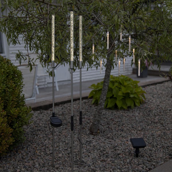 Gartenszene mit Solarleuchten in Rohrform und als Hängeleuchten an einem Baum.