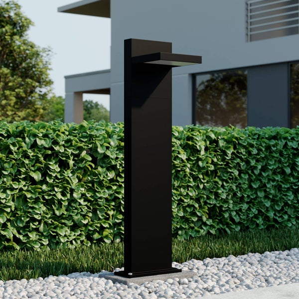 Moderne schwarze Wegeleuchte in einem Garten vor einer grünen Hecke und einem modernen Wohnhaus.