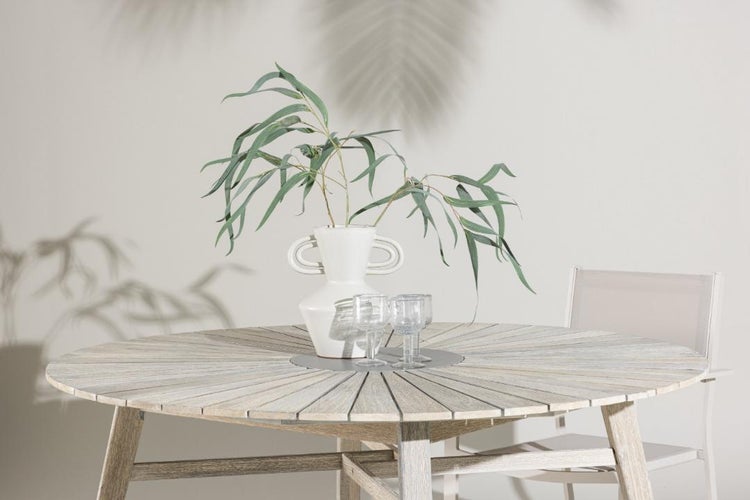 Runder Gartentisch aus Holz mit fächerförmig angeordneten Lamellen, darauf eine weiße Vase mit Zweigen und Gläser.