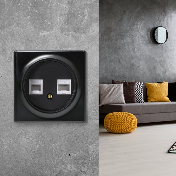 Doppel-Netzwerkdose mit zwei Anschlüssen für Datenkabel an einer Wand, daneben ein moderner Wohnbereich mit Sofa und Dekokissen.