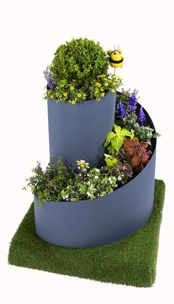 Spiralförmiges Hochbeet aus Metall, bepflanzt mit verschiedenen Blumen und Sträuchern, inklusive dekorativer Bienen, auf Kunstrasen stehend.