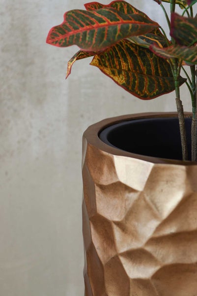 Nahaufnahme eines dekorativen Blumentopfs mit geometrischer Oberflächenstruktur und einer Zimmerpflanze.