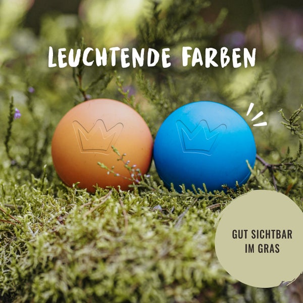 Zwei Hundespielbälle mit Kronenmuster im Gras
