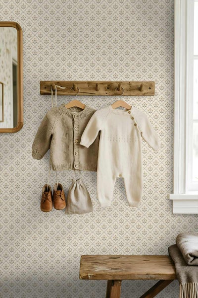 Kinderzimmer mit gemusterter Tapete mit kleinen floralen Motiven, einer hölzernen Garderobe mit Babykleidung und einem Spiegel.