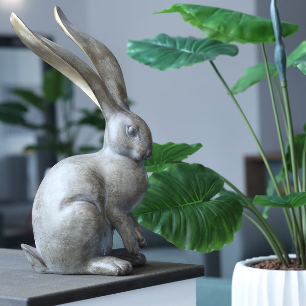 Dekorativer Hase aus Kunststein neben einer Topfpflanze als Gartendekoration.