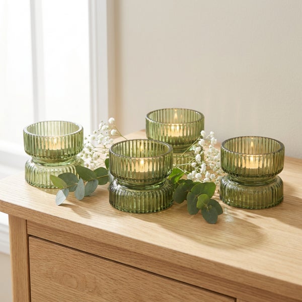 Set aus vier geriffelten Teelichthaltern aus Glas mit Kerzen auf einer Holzkommode dekoriert mit Schleierkraut und Eukalyptuszweigen.