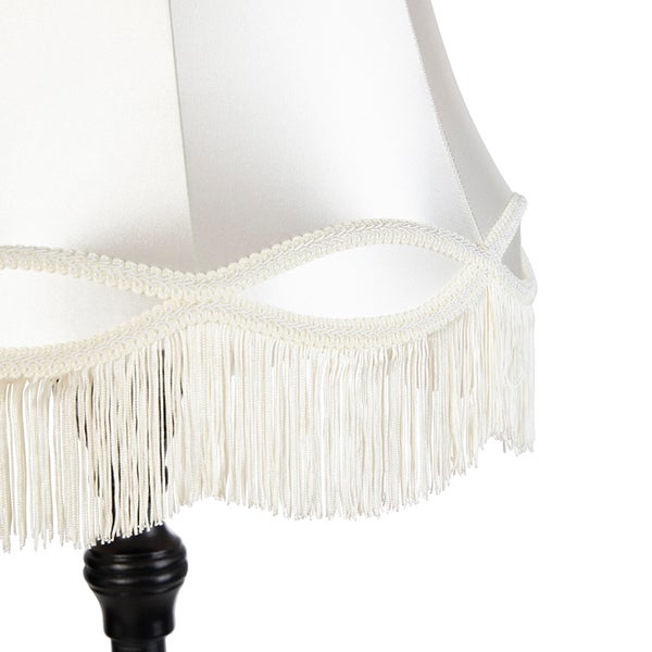 Detailaufnahme eines weißen Textillampenschirms mit dekorativer Borte und Fransen auf einem dunklen Lampenfuß.