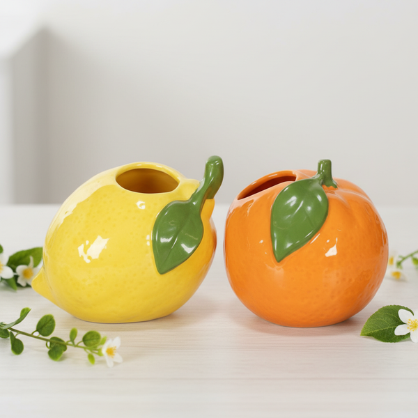Zwei Keramik-Pflanztöpfe in Form einer gelben Zitrone und einer orangefarbenen Orange mit grünen Blättern.