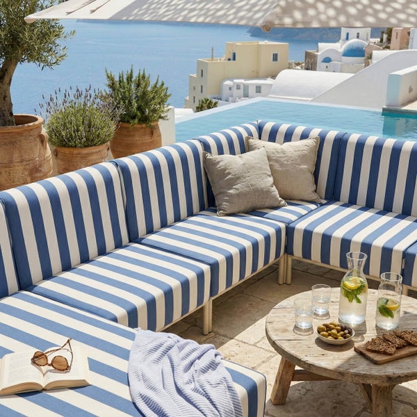 Outdoor-Lounge-Set mit blau-weiß gestreiftem Sofa, Holz-Couchtisch und Terrakotta-Töpfen auf einer Terrasse mit Pool und Meerblick.