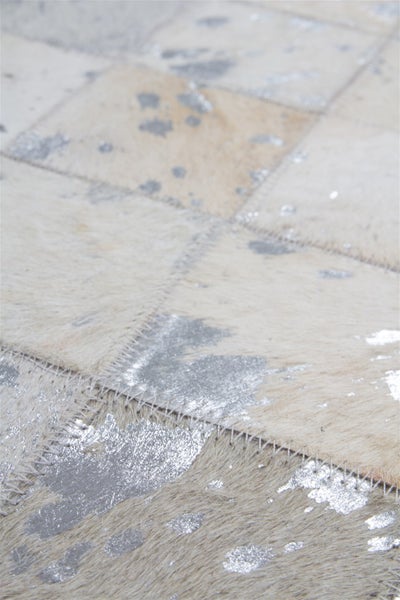 Patchwork-Teppich aus Kuhfell mit silbernen Metallic-Effekten und sichtbaren Nähten.