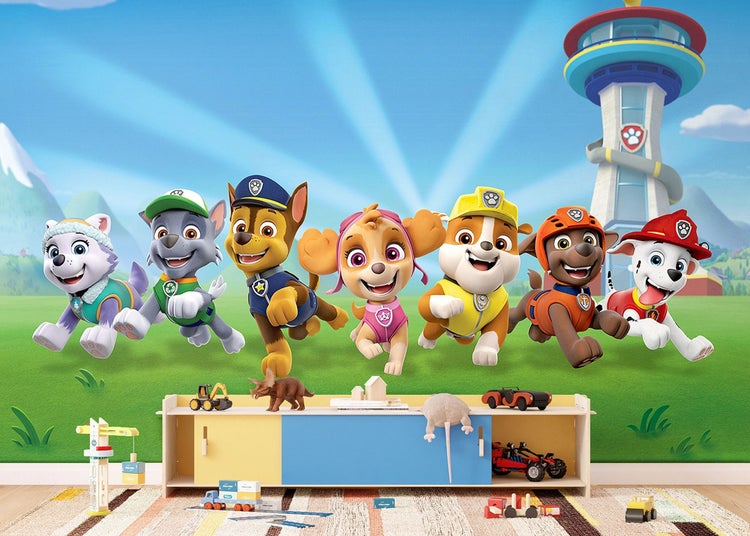 Paw Patrol Fototapete im Kinderzimmer mit Charakteren auf einer Wiese vor der Zentrale, über einer Kommode mit Spielzeug.