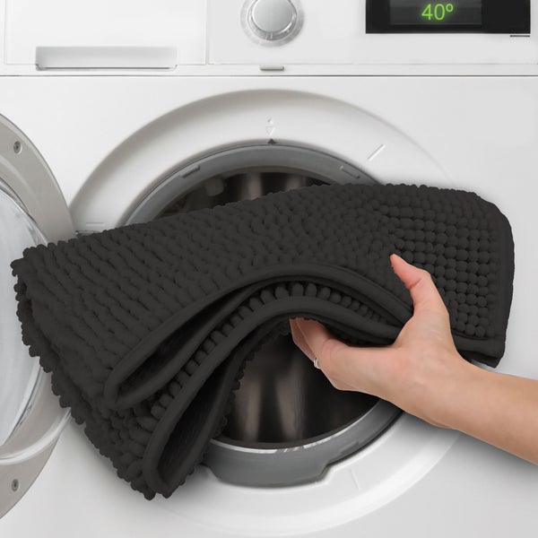 Eine Person legt eine Badematte in eine Waschmaschine. Die Temperaturanzeige der Waschmaschine zeigt 40 Grad.