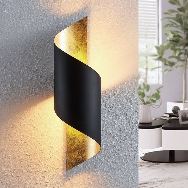 Moderne Wandleuchte aus Metall in Schwarz und Gold mit indirekter Beleuchtung, geschwungene Form an einer strukturierten Wand.