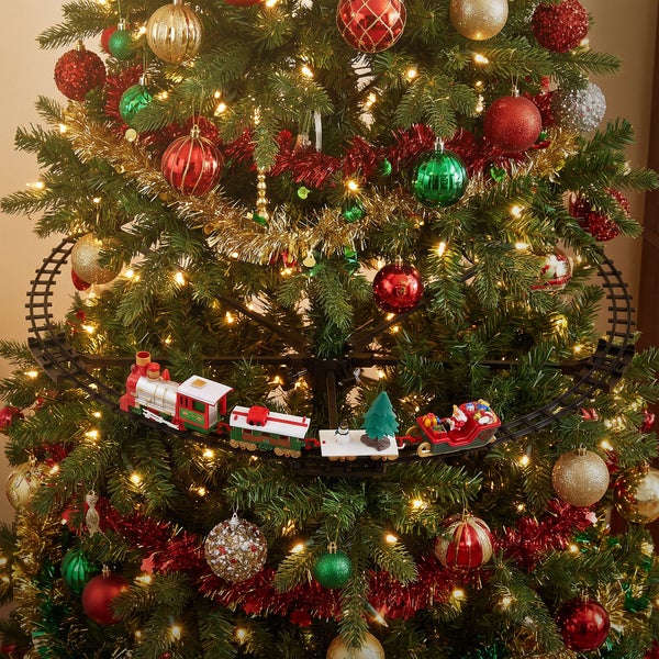 Weihnachtsbaum mit elektrischer Spielzeugeisenbahn auf den Zweigen montiert, geschmückt mit Kugeln und Lichterkette.
