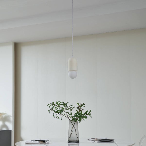 Moderne Pendelleuchte mit Keramikfassung und Glasbirne über einem hellen Esstisch mit Vase und grünen Zweigen.