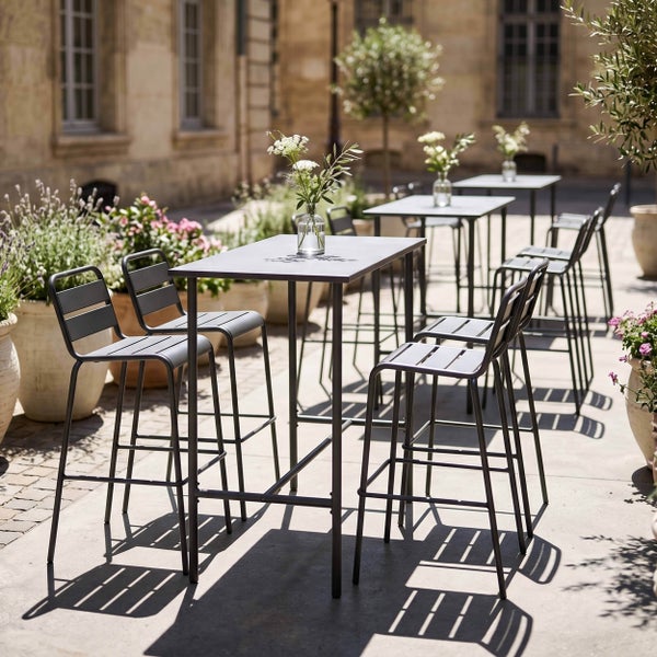 Moderne Außenbestuhlung mit Stehtischen aus anthrazitfarbenem Metall und passenden Barhockern auf einer hellen, bepflanzten Terrasse.