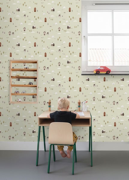 Vliestapete im Kinderzimmer mit Häuser- und Baummuster, dazu ein Schreibtisch aus Holz und ein Wandregal mit Spielzeugautos.