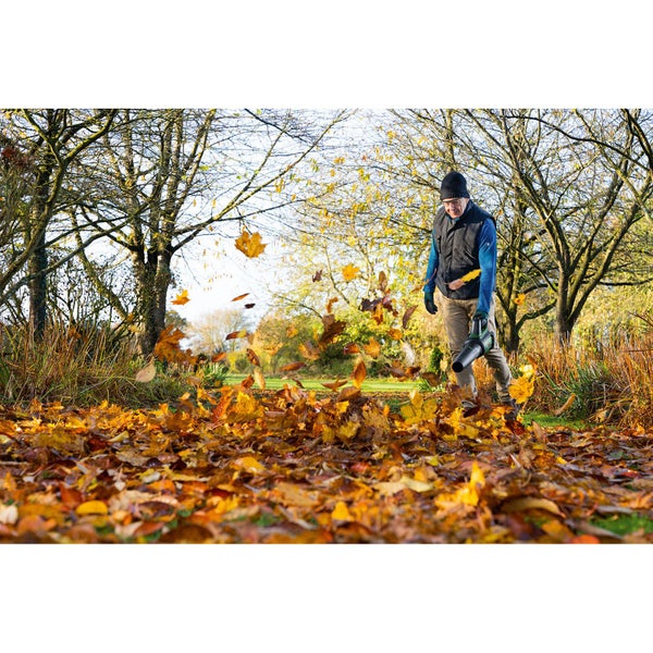 Mann benutzt Laubbläser im Garten, um Herbstlaub zu entfernen