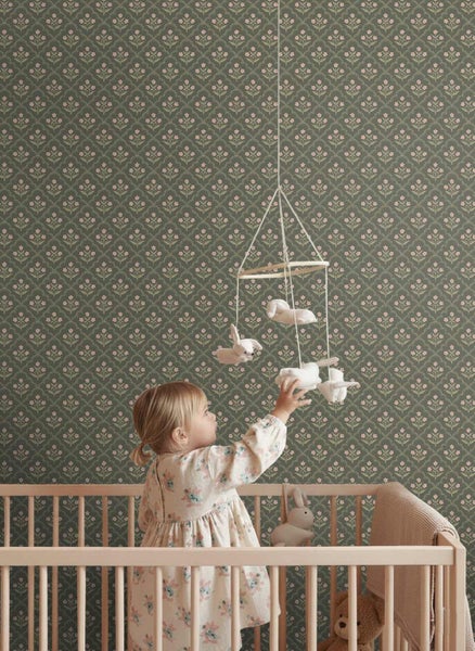 Ein Kind im hölzernen Gitterbett in einem Kinderzimmer mit Vliestapete mit floralem Muster an der Wand.